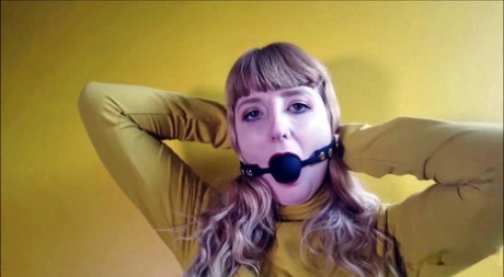 Fully dressed girl fits her mouth with a black ball gag on a couch 14163720
